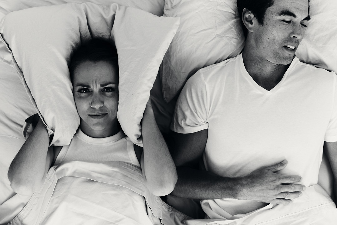 Woman covering her ears while man snores.