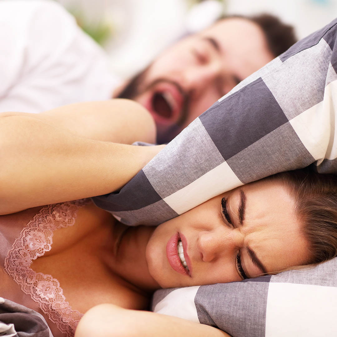 A man snoring and woman covering her ears.