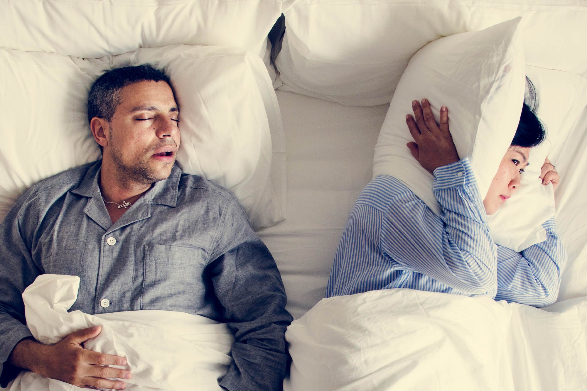 Man snoring in bed, wife covering her ears.