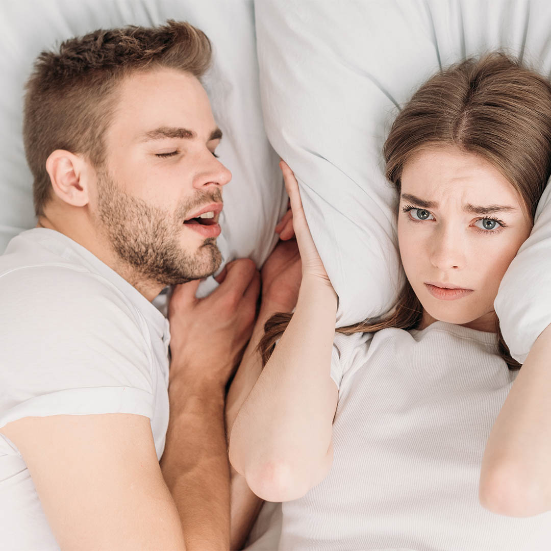 A man snoring, while a woman covers her ears.