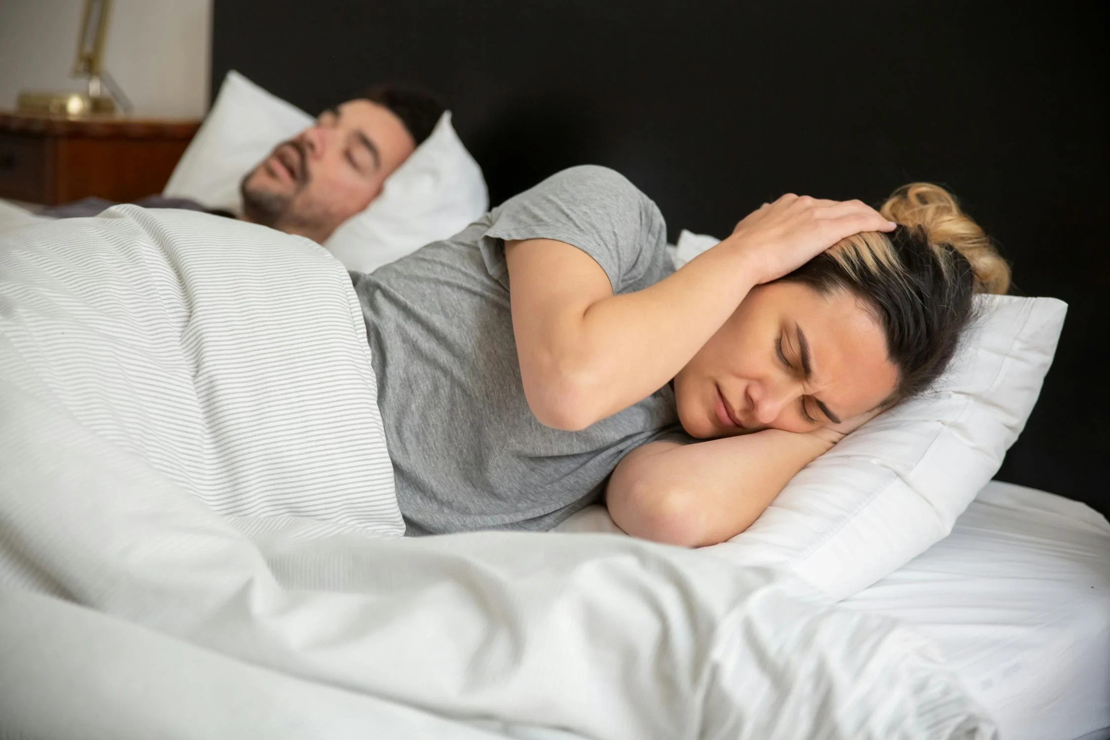 Couple man snoring, woman covering her ears.